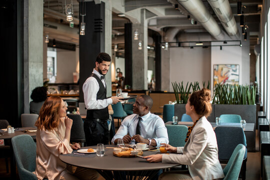 Diverse business people meeting in hotel restaurant with waiter serving