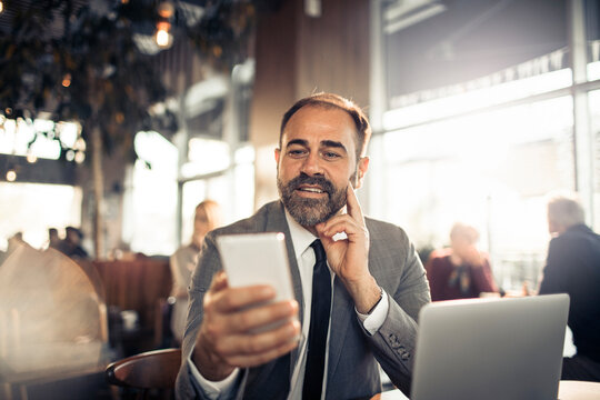 Smiling businessman using smartphone and laptop at cafe