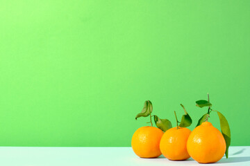Three clementines citrus fruit against a green and blue colored background
