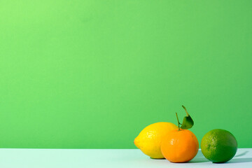 Lemon, lime and clementine citrus fruits against a green and blue colored background