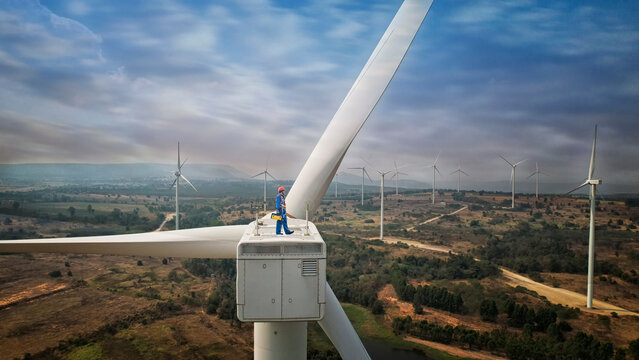 Windmill engineer wearing PPE standing on wind turbine.  engineer feel success after good work. He standing a top of windmill.