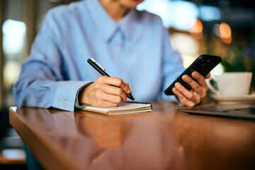 A female restaurant manager is working, holding a phone and writing notes.