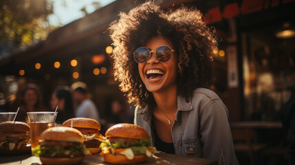 Young girl eating classic burger with friends at cafe in the city. Smiling beautiful young happy...