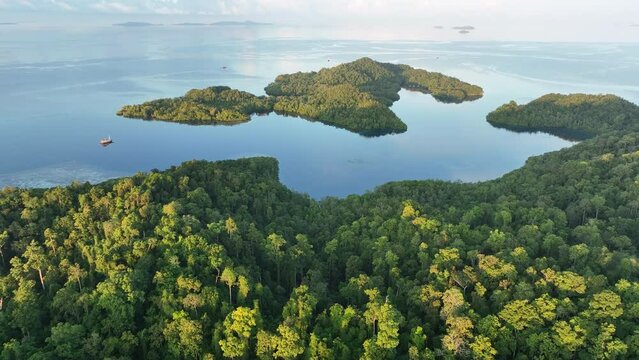 Early sunlight illuminates calm seas around the islands of Gam and Yangeffo in Raja Ampat, Indonesia. This region is mostly known for its exquisite coral reefs and overall high marine biodiversity.