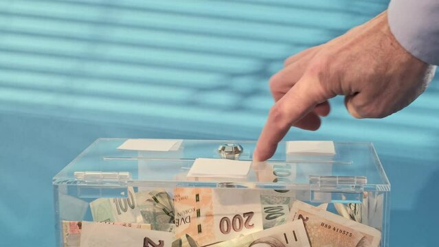 Hand give Charity and money CZK czech koruna banknotes to a transparent donation box for money donation. A financial support, collects money for a f giving supports charitable initiatives.