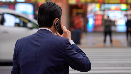 A Japanese businessman stands patiently in crosswalk, using a smartphone in hand