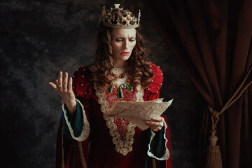unhappy medieval queen in red dress with parchment and crown