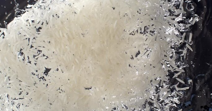 Super slow motion of dry basmati quality white rice is falling in pot with boiling water to be cooked with traditional recipes for dietetic vegetarian dish preparation by chef in restaurant kitchen.