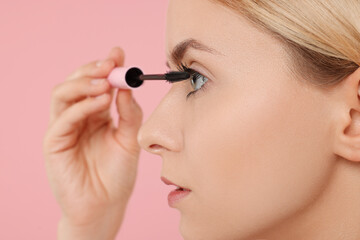 Beautiful woman applying mascara on pink background, closeup