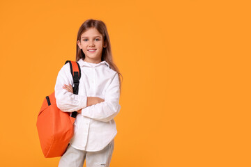 Happy schoolgirl with backpack on orange background. Space for text