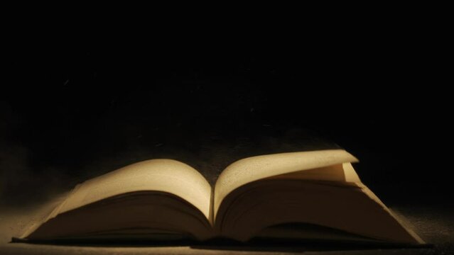Close up studio shot of old retro hardcover book on dark background in warm light. Old vintage book laying,wind turning pages.