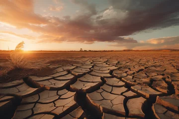 Deurstickers The sun sets dramatically over a vast landscape of dry, cracked soil, evoking the severity of drought conditions.  © Kamonwan