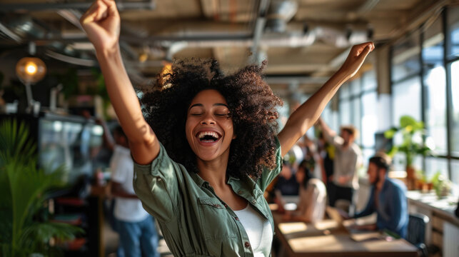 Group of people are celebrating in an office environment, with one woman in the center laughing and raising her arms in joy, surrounded by her colleagues who are also expressing happiness.