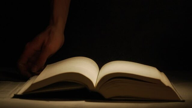 Close up studio shot of old retro hardcover book. on dark background in warm light. Man close old book, cloud of dust in the air.