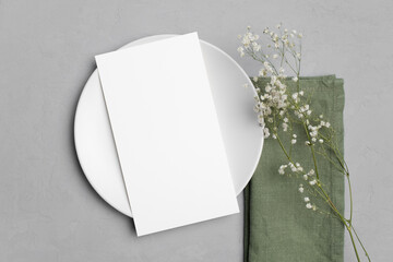 Wedding blank menu card mockup on white plate with napkin and gypsophila flowers, top view, copy...