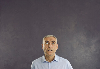 Pensive serious middle-aged Caucasian man on black studio background look up at blank empty copy space. Pensive male think consider advertising sale deal or promotion discount. Copyspace, ad.
