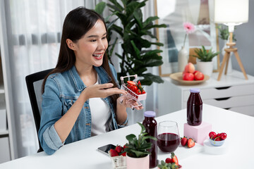 Smiling young beautiful Asian reviewing tasty mixed strawberry and cherry juice detox drinks,...