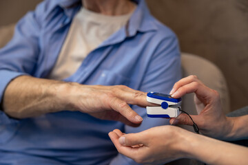 Nurse checking pulse or level of oxygen using oximeter of unrecognizable senior man.