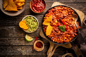 Mexican hot chili con carne in a pan with tortilla chips on dark background, top view - obrazy, fototapety, plakaty
