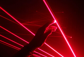 close-up hand touching the red line of a laser beam in a dark room.
