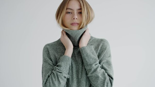 Young attractive female model in soft knitted sweater posing on camera and smile in studio with white background. charming woman in warm stylish clothes. Fashion concept