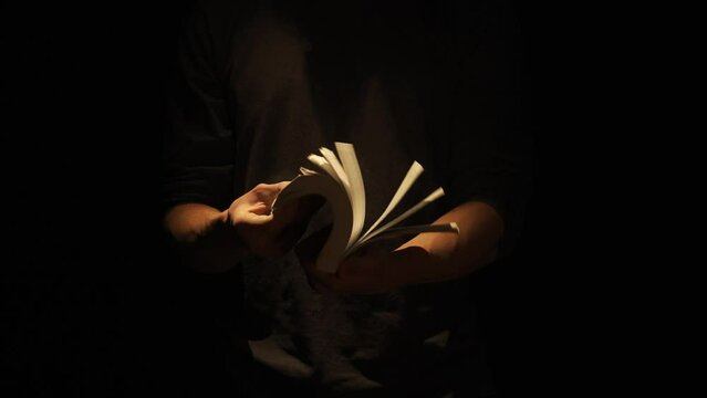 Close up studio shot of male with retro book on dark background in warm light. Man holding turning fast pages of old dusty book.