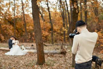 Professional wedding photographer taking pictures of the bride and groom in nature in autumn