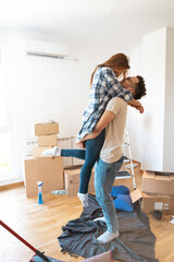 Young man lifting woman in their new home. They are dressed casually and having a lot of unpacked...