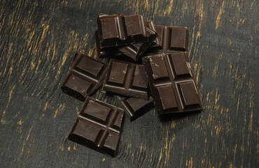 pieces of chocolate bar on a dark wooden background. dark photo. broken chocolate bar.