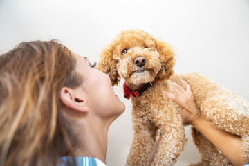 Happy young woman lifting dog up. Female pet owner with a brown poodle.