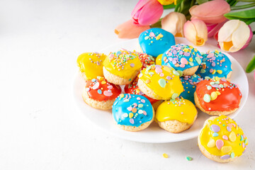 Fototapeta na wymiar Homemade Italian Easter cookies with colorful sugar glaze and sprinkles, on white kitchen table background, decorated with Easter holiday decor and spring tulip flower bouquet 