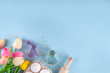 Easter baking background, ingredient for making Easter cookies, cakes, dessert with Easter chocolate eggs, sugar sprinkles, baking ingredients, flour, egg, milk, rolling pin, spring flowers top view