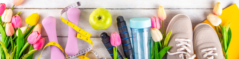 Spring sport fitness background. Outdoors springtime workouts concept. Running sneakers, dumbbell, jump rope, water bottle, tape measure, spring tulip flower, wooden background top view copy space
