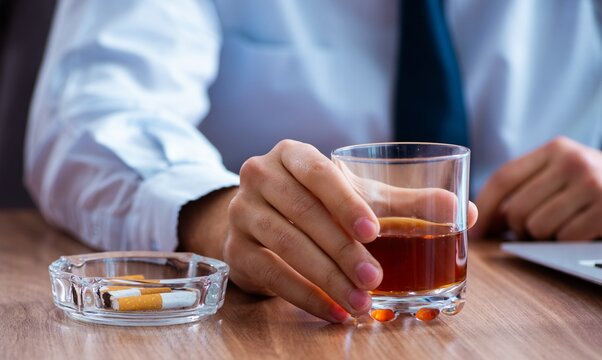 Male employee drinking alcohol and smoking cigarettes at workpla