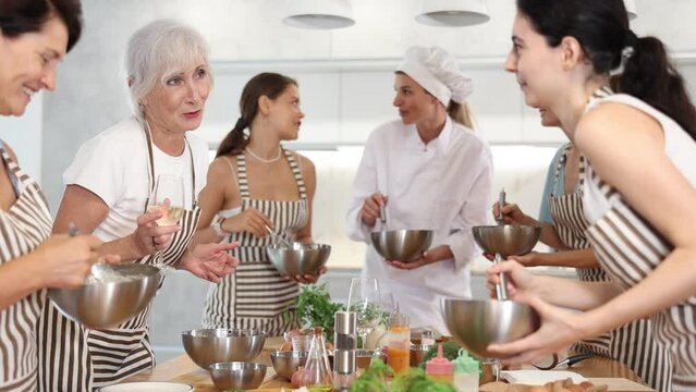 Elderly woman holds glass of cool white wine in hands and converse with participant at culinary courses. High quality 4k footage