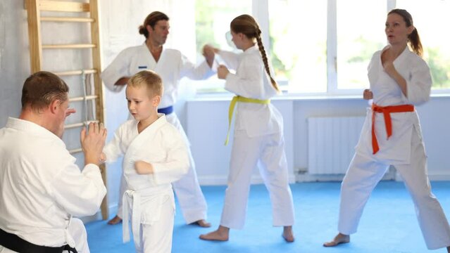Boy is paired with man teacher to learn how to strike and rehearses blocking opponent, using karate technique