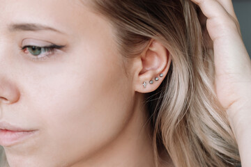 Ear piercing. Cropped shot of a young blonde woman wearing four stud earrings on the earlobe....