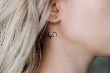 Temporary mini tattoo in the form of a heart and a cardiogram on the young woman's neck under ear