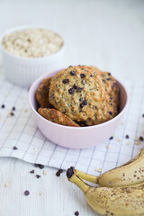 Homemade oat cookies with chicilate chips and bananas in pink bowl on white background close up selective focus