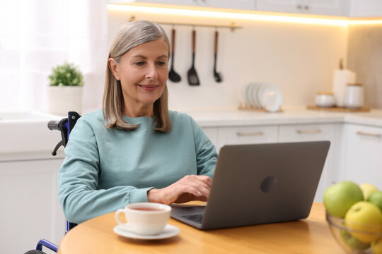 Woman in wheelchair using laptop at table in home office