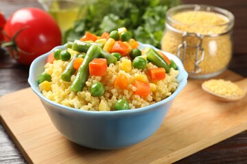 Tasty millet porridge with vegetables in bowl on wooden table, closeup