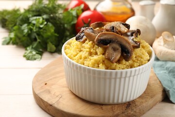 Tasty millet porridge and mushrooms in bowl on light wooden table, closeup. Space for text