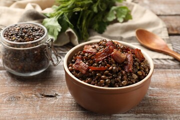 Delicious lentils with bacon in bowl on wooden table, closeup