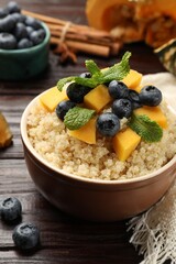 Tasty quinoa porridge with blueberries, pumpkin and mint in bowl on wooden table, closeup