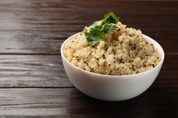 Tasty quinoa porridge with parsley in bowl on wooden table, closeup. Space for text