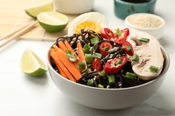 Tasty buckwheat noodles (soba) with chili pepper, egg, carrot and mushrooms in bowl on white marble table, closeup