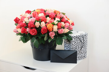 Bouquet of beautiful roses, envelope and shopping bag on white drawer unit