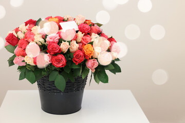 Bouquet of beautiful roses with blank card on white table against light background, space for text