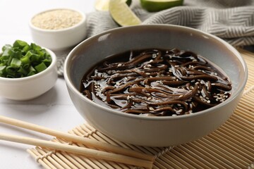 Tasty buckwheat noodles (soba) with sauce in bowl and chopsticks on white table, closeup