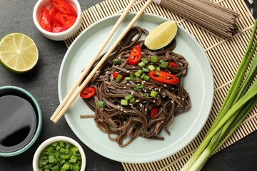 Tasty buckwheat noodles (soba) with ingredients and chopsticks on grey table, flat lay